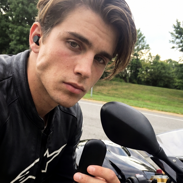 a young male rider holding a earplug case and wearing the blok. riders V2 earplug with a BMW motorbike in an outdoor setting