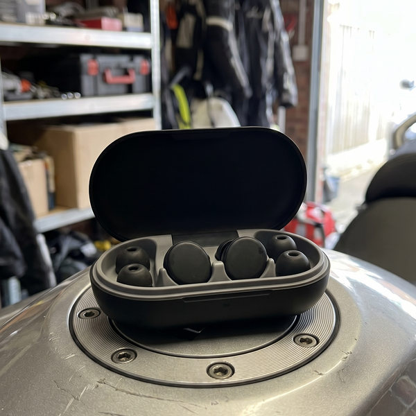 Blok. riders V2 earplugs and earplug case sitting on top of a motobike fuel tank in a garage with work gear surrounding.
